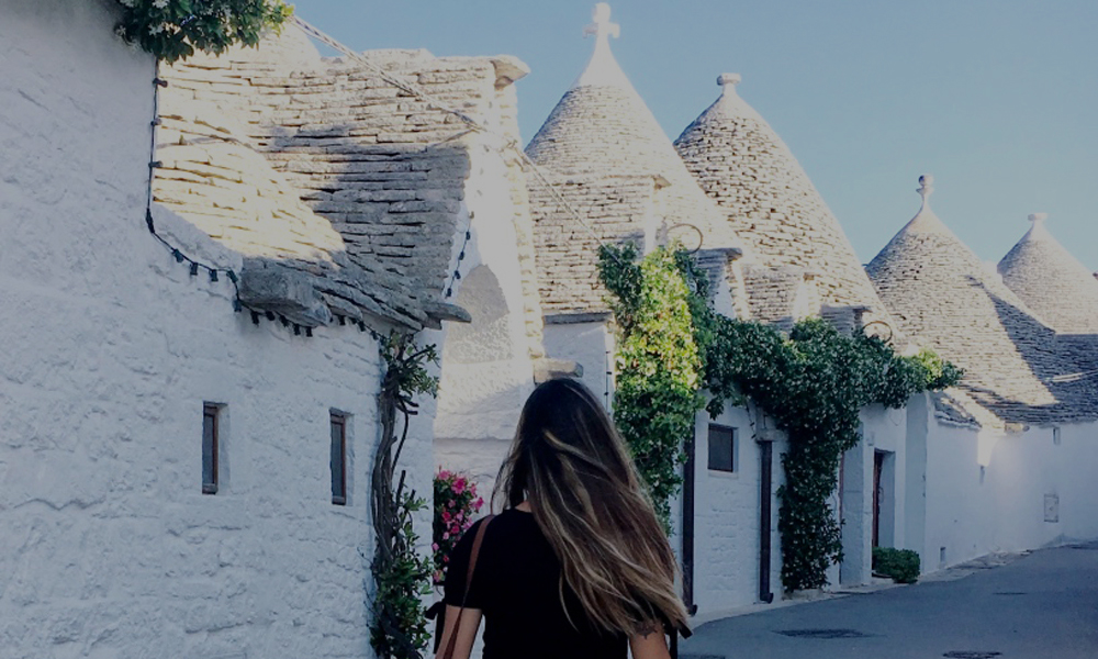 Una via del Rione Monti ad alberobello con trulli sullo sfondo e soggetto di spalle in primo piano