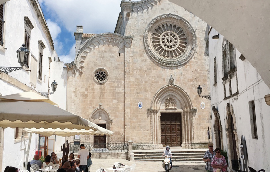 Il Duomo di Ostuni visto da dietro un'arco. Soggetto in vespa in lontananza