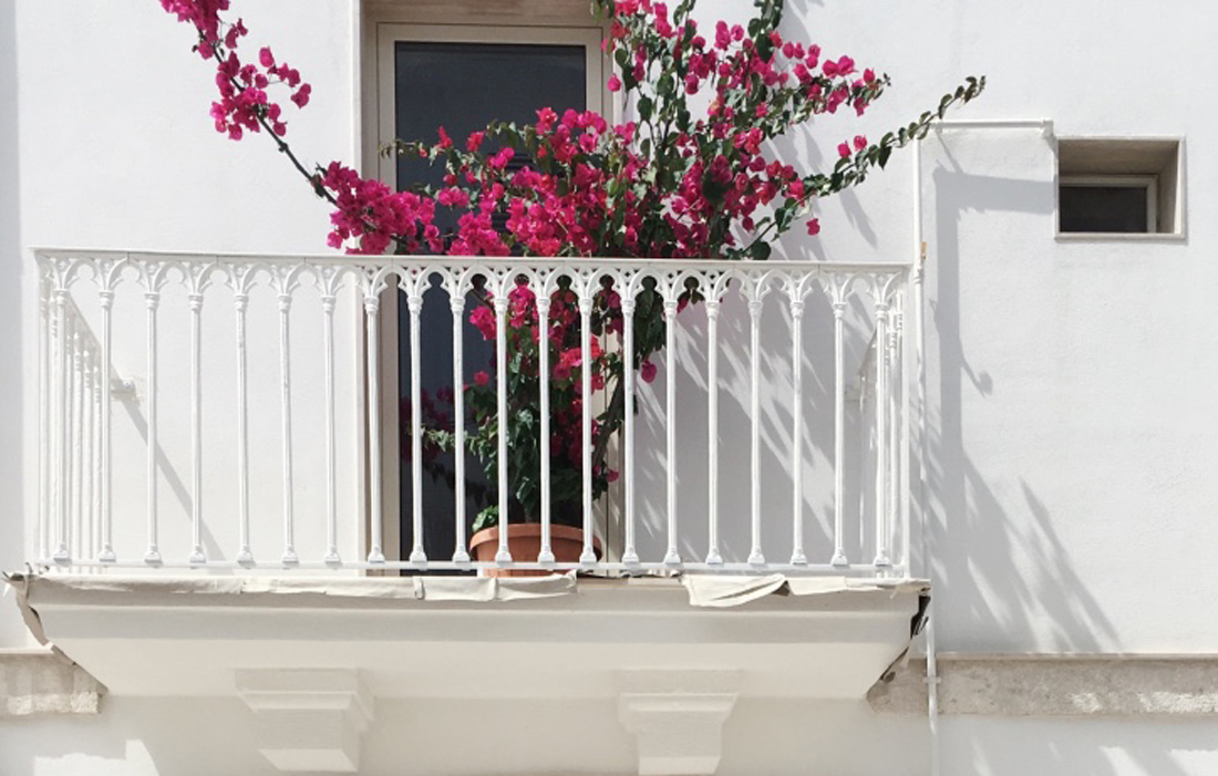 Un caratteristico balconcino bianco ornato da fiori rosa fucsia a Polignano a Mare