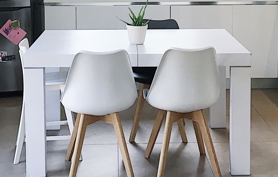 Tavolo in legno bianco con sedie con zampe in legno chiaro. Sul tavolo una pianta verde su vaso di ceramica